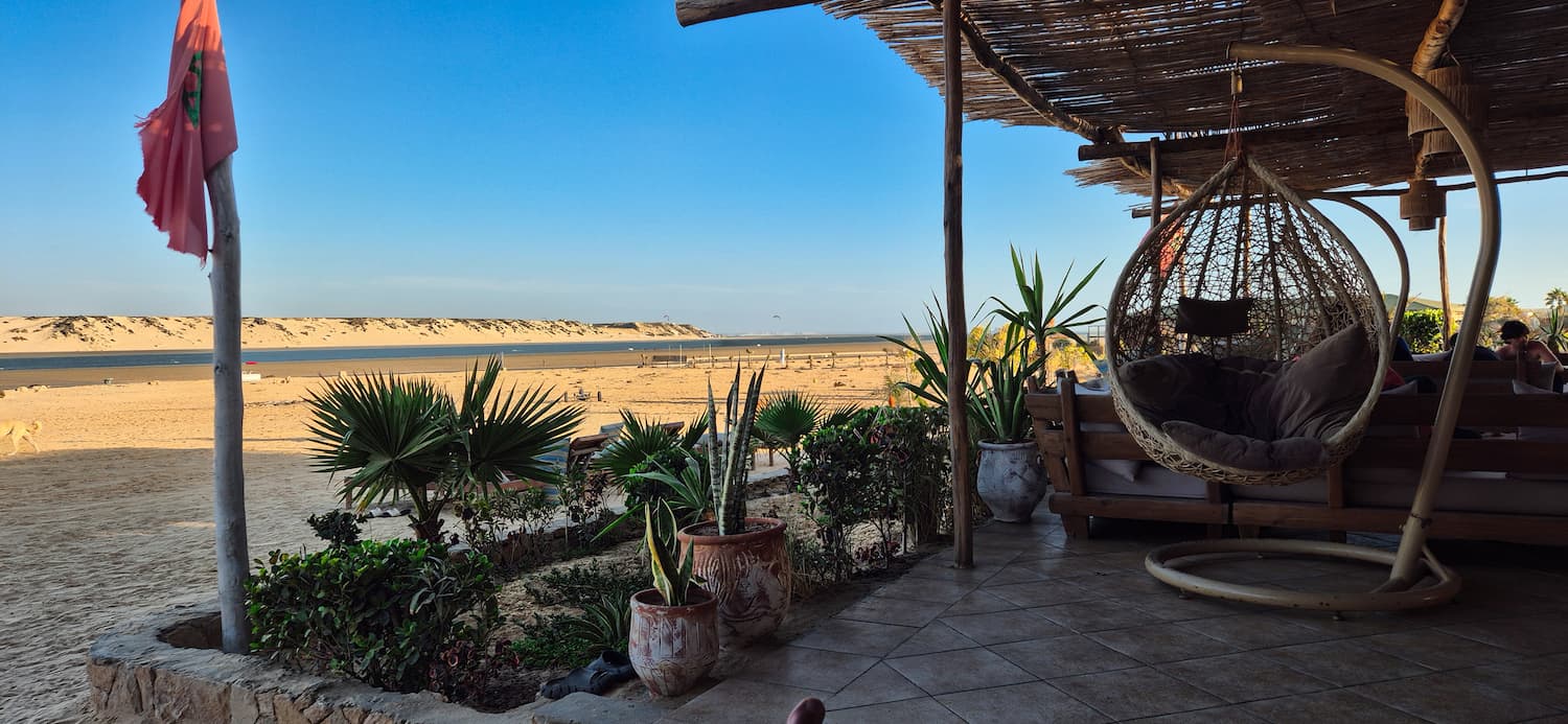 Rolig morgenstemning på den hyggelige udendørs terrasse med kurve-hængestol på Auberge des Nomades du Sahara med den åbne sandstrand i baggrunden