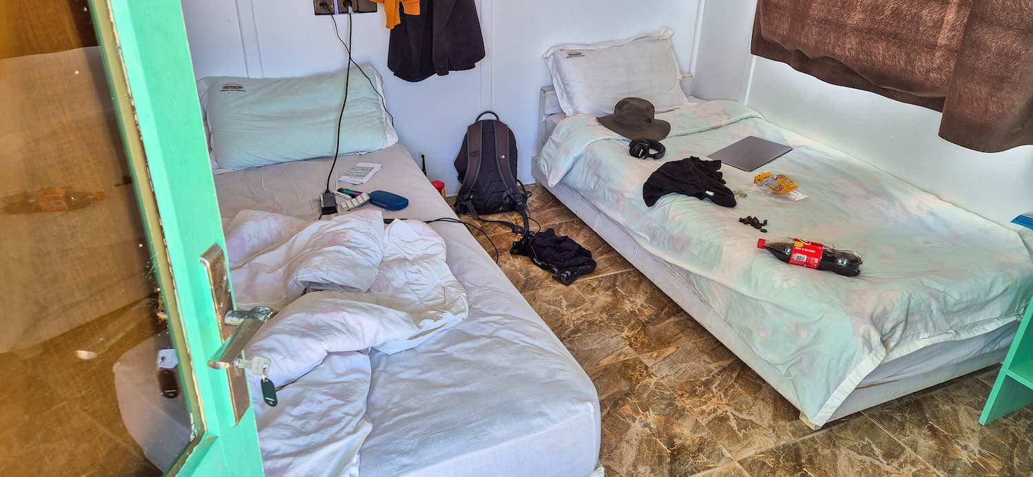 Indenfor i et af de simple, delte værelser med to opredte senge, rygsæk og personlige ejendele på Auberge des Nomades du Sahara.